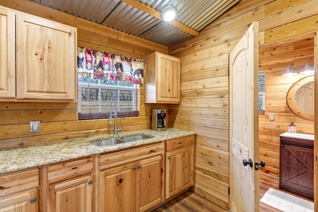 kitchen featuring light stone counters, light brown cabinetry, sink, and wood walls