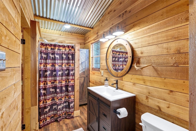 bathroom featuring vaulted ceiling, wood walls, hardwood / wood-style flooring, vanity, and toilet