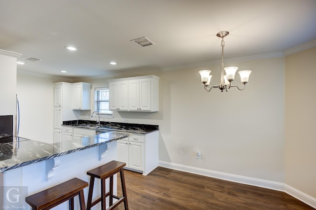 kitchen featuring dark wood-type flooring, white cabinetry, crown molding, dark stone countertops, and pendant lighting