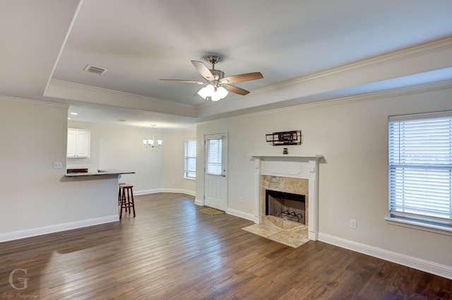 unfurnished living room featuring ceiling fan with notable chandelier, a high end fireplace, a tray ceiling, crown molding, and dark wood-type flooring