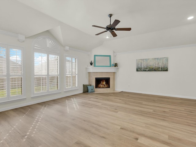 unfurnished living room with ceiling fan, vaulted ceiling, a tile fireplace, and light hardwood / wood-style flooring