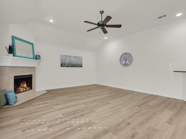 unfurnished living room featuring crown molding, vaulted ceiling, ceiling fan, a tiled fireplace, and light hardwood / wood-style floors