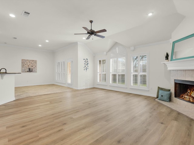 unfurnished living room featuring light hardwood / wood-style flooring, ceiling fan, ornamental molding, a tiled fireplace, and vaulted ceiling