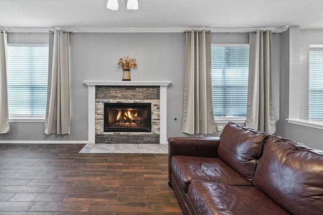 living room featuring dark wood-style floors, a stone fireplace, and baseboards