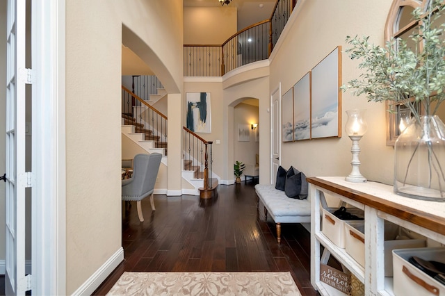 foyer entrance featuring baseboards, arched walkways, a towering ceiling, wood finished floors, and stairs