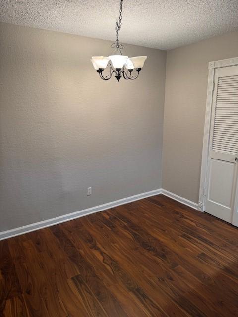 unfurnished room with a chandelier, a textured ceiling, and dark hardwood / wood-style flooring