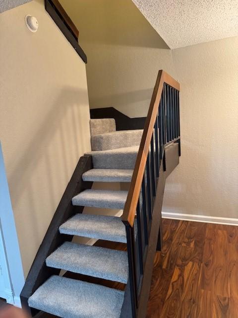 stairs with wood-type flooring and a textured ceiling