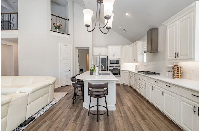 kitchen featuring white cabinetry, appliances with stainless steel finishes, an island with sink, pendant lighting, and wall chimney range hood