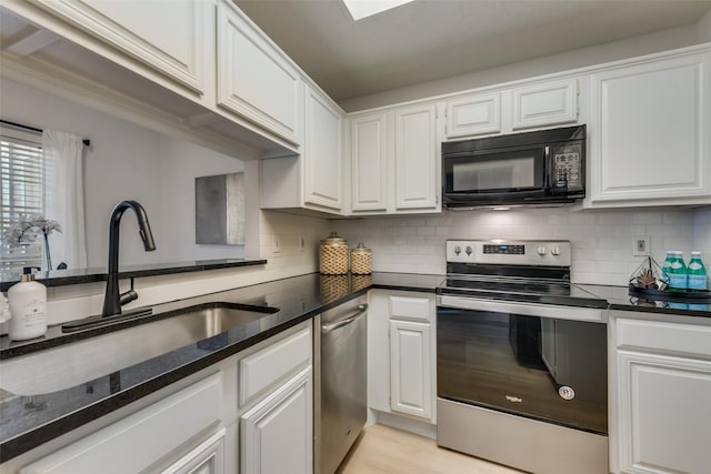 kitchen with appliances with stainless steel finishes, tasteful backsplash, sink, dark stone countertops, and white cabinets