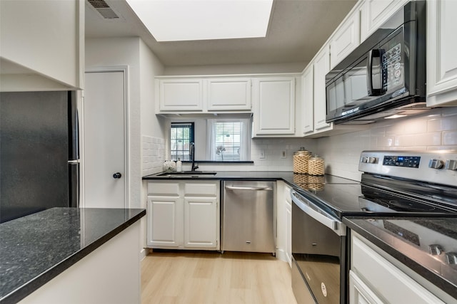 kitchen featuring sink, black appliances, light hardwood / wood-style flooring, dark stone counters, and white cabinets