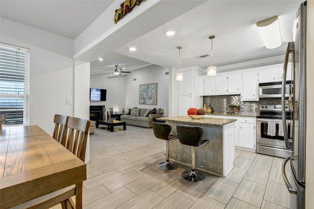 kitchen with white cabinets, hanging light fixtures, a center island, stainless steel appliances, and light stone countertops