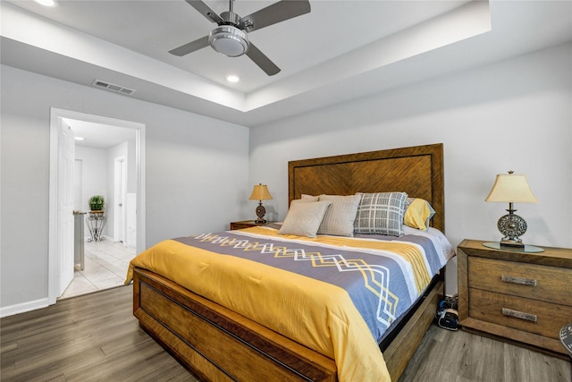 bedroom with wood-type flooring, a raised ceiling, and ceiling fan