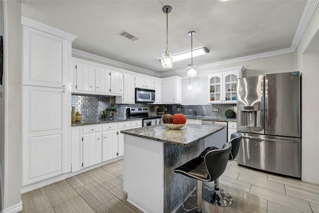 kitchen featuring appliances with stainless steel finishes, dark stone countertops, backsplash, a center island, and white cabinets