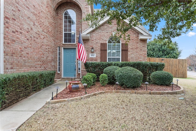 view of exterior entry featuring brick siding and fence