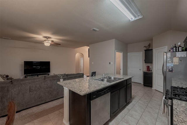 kitchen featuring sink, an island with sink, ceiling fan, stainless steel appliances, and light stone countertops