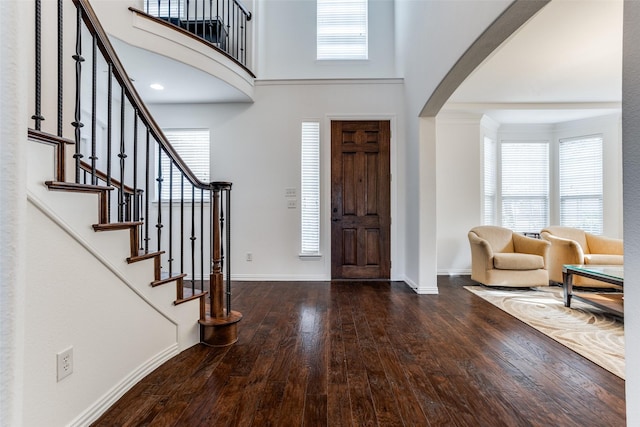 foyer entrance featuring a towering ceiling, dark wood-type flooring, and plenty of natural light