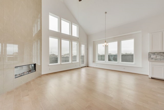 unfurnished living room with a tile fireplace, a chandelier, high vaulted ceiling, and light wood-style floors