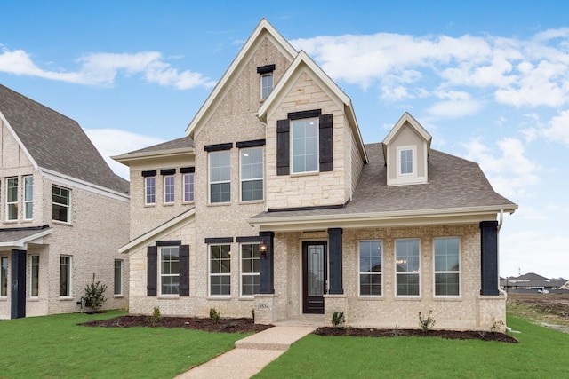 view of front facade featuring a front yard, roof with shingles, and stone siding