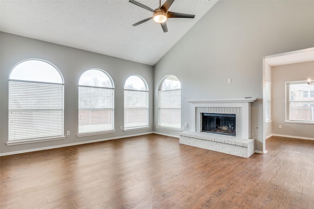 unfurnished living room featuring dark wood-type flooring, high vaulted ceiling, a textured ceiling, ceiling fan, and a fireplace