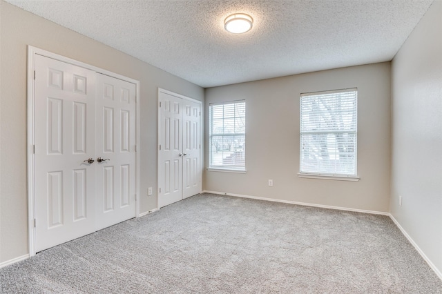 unfurnished bedroom featuring multiple windows, two closets, light colored carpet, and a textured ceiling