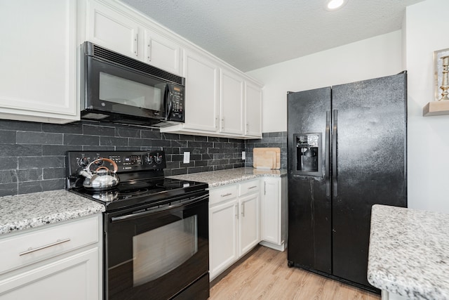 kitchen with light stone counters, black appliances, light hardwood / wood-style floors, and white cabinets