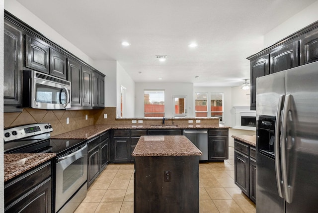 kitchen with tasteful backsplash, a kitchen island, dark stone counters, appliances with stainless steel finishes, and a sink