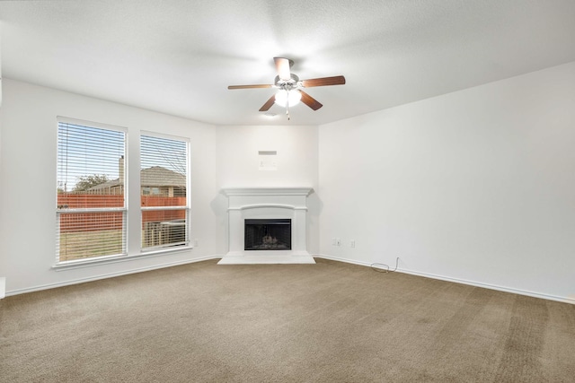 unfurnished living room with a fireplace with raised hearth, baseboards, a ceiling fan, and carpet floors