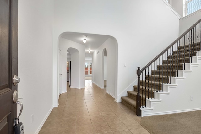 entrance foyer featuring baseboards, arched walkways, a towering ceiling, and light tile patterned flooring