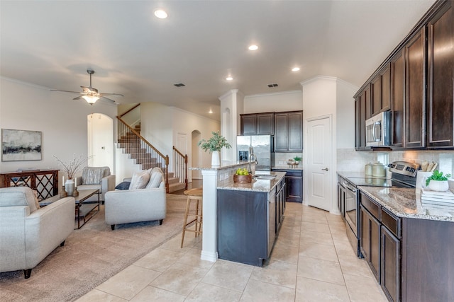 kitchen with open floor plan, a breakfast bar, light stone counters, arched walkways, and stainless steel appliances