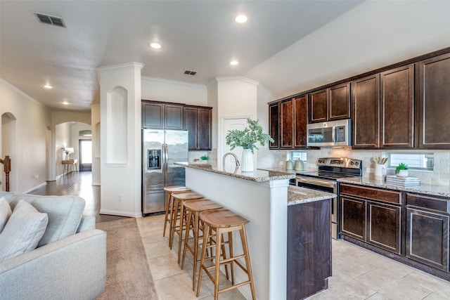 kitchen with tasteful backsplash, visible vents, dark brown cabinetry, a breakfast bar, and stainless steel appliances