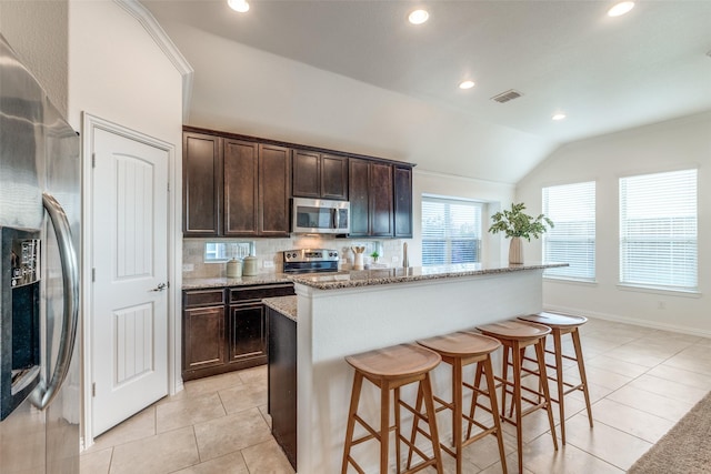 kitchen with visible vents, lofted ceiling, dark brown cabinets, appliances with stainless steel finishes, and tasteful backsplash