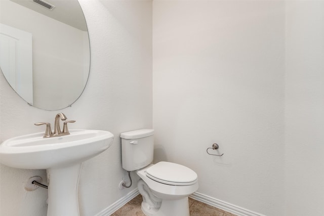 half bath featuring visible vents, baseboards, a sink, tile patterned flooring, and toilet