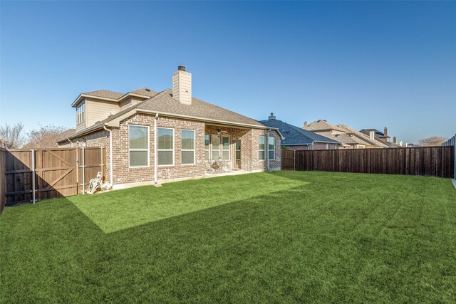 rear view of house featuring roof with shingles, a fenced backyard, a chimney, a lawn, and brick siding