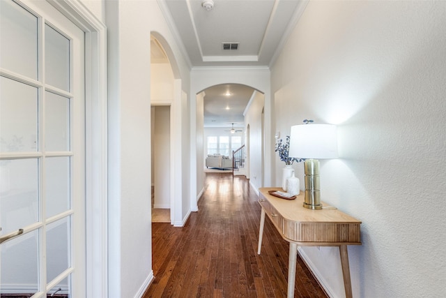 hallway featuring dark wood-style floors, visible vents, baseboards, arched walkways, and crown molding