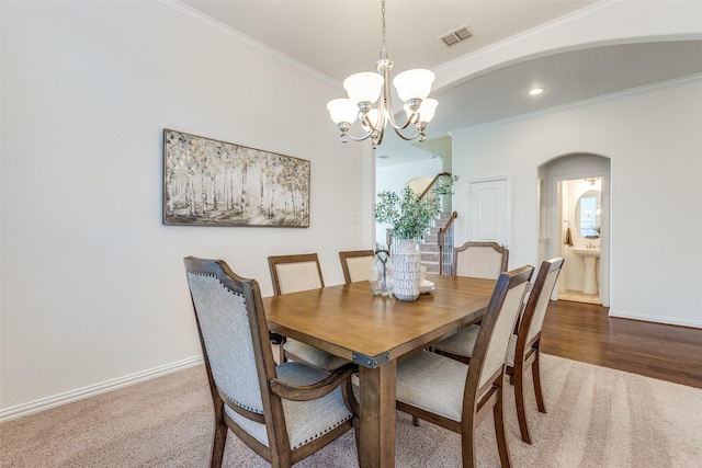 carpeted dining room with visible vents, baseboards, arched walkways, crown molding, and a chandelier