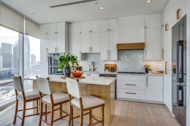 kitchen featuring sink, black cooktop, high end refrigerator, light wood-type flooring, and white cabinets