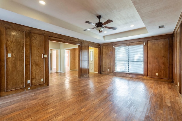 interior space featuring ceiling fan, visible vents, wood finished floors, baseboards, and a tray ceiling