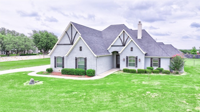 tudor home featuring a shingled roof, brick siding, a chimney, and a front lawn