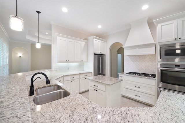 kitchen with arched walkways, crown molding, custom exhaust hood, appliances with stainless steel finishes, and a sink