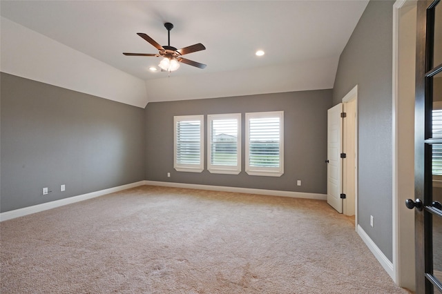 spare room with light colored carpet, vaulted ceiling, baseboards, and ceiling fan