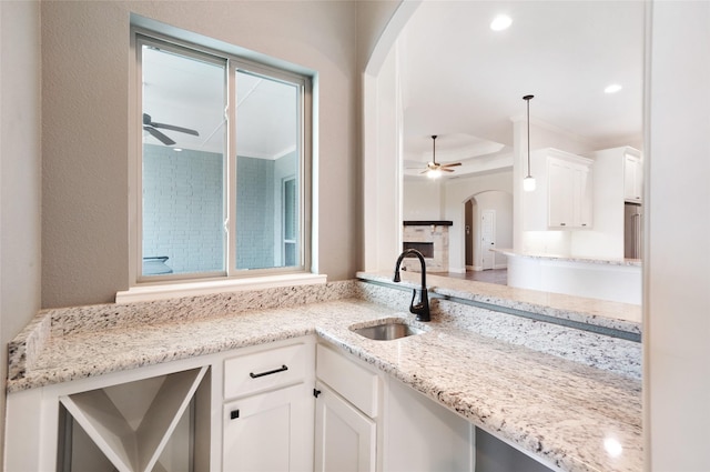 kitchen with arched walkways, white cabinetry, a sink, and ceiling fan