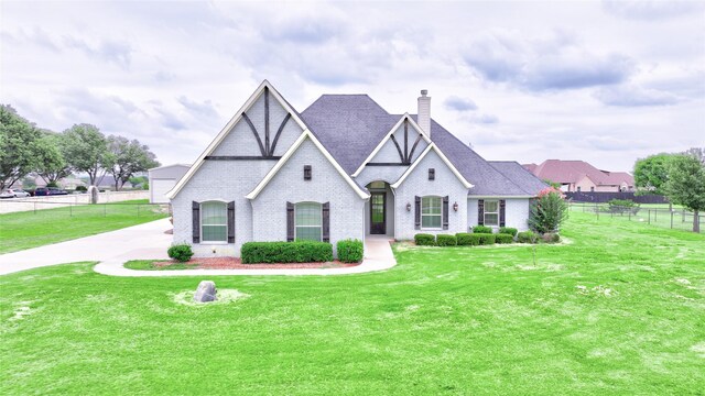 english style home featuring a chimney, a front yard, and fence