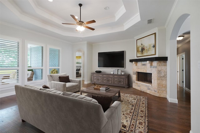 living area with dark wood-type flooring, arched walkways, a fireplace, and a tray ceiling