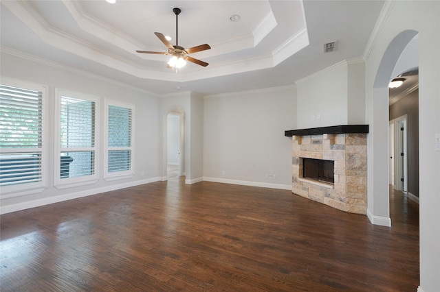 unfurnished living room with visible vents, arched walkways, ceiling fan, a tray ceiling, and a fireplace