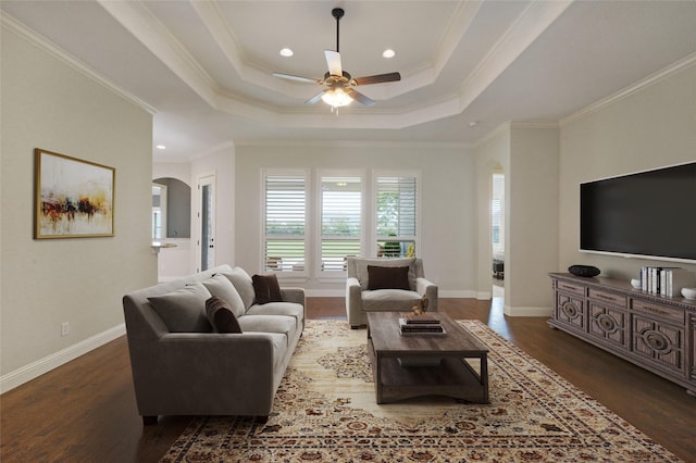 living room featuring baseboards, arched walkways, a tray ceiling, and wood finished floors