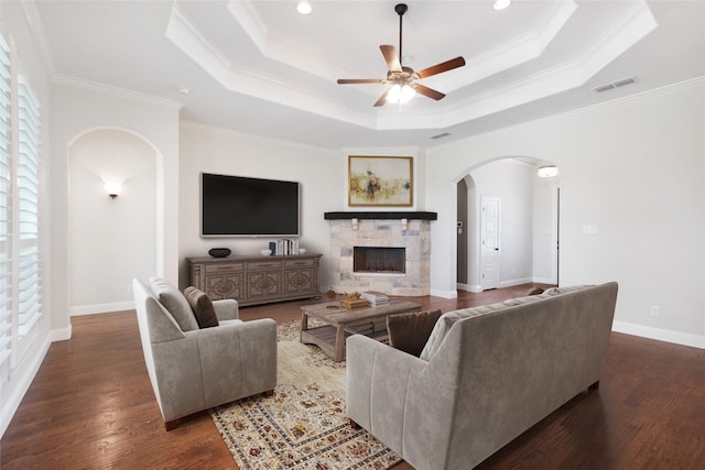 living room featuring a tray ceiling, a fireplace, visible vents, wood finished floors, and baseboards