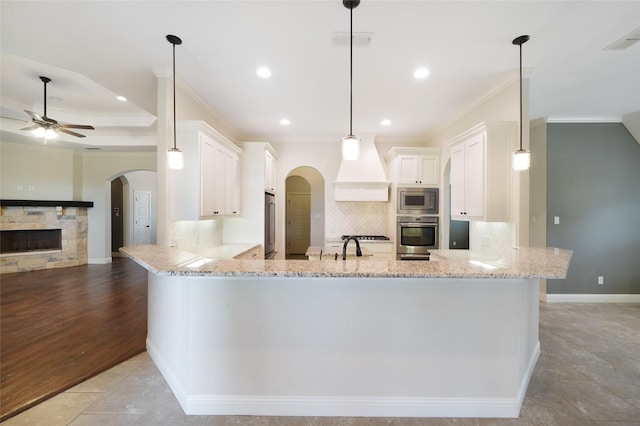 kitchen featuring arched walkways, a stone fireplace, appliances with stainless steel finishes, and a peninsula