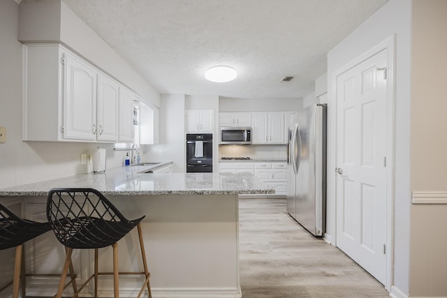 kitchen with light stone counters, white cabinetry, a kitchen breakfast bar, stainless steel appliances, and kitchen peninsula