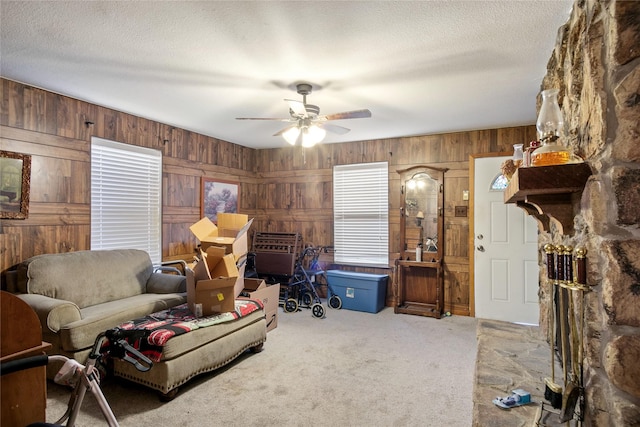 living room featuring ceiling fan, carpet flooring, a textured ceiling, and wood walls