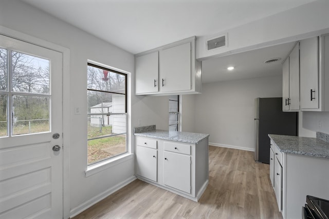 kitchen featuring visible vents, freestanding refrigerator, light stone countertops, white cabinetry, and a wealth of natural light